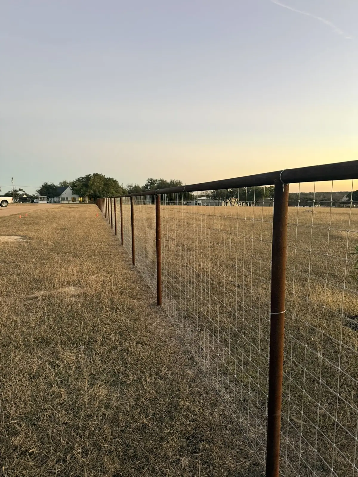 Pipe post and wire ranch fence line at sunset